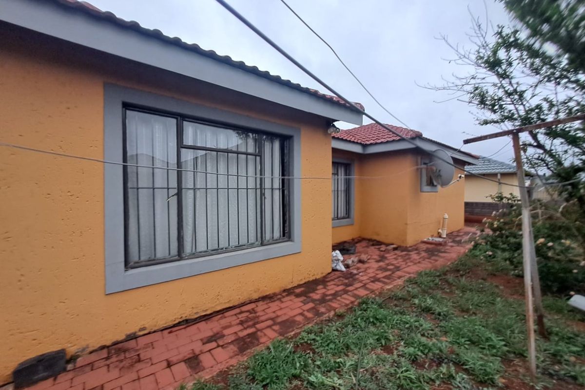 Rear exterior view of the house featuring plastered walls, tiled roof, and brick paved walkway leading along the side of the property.