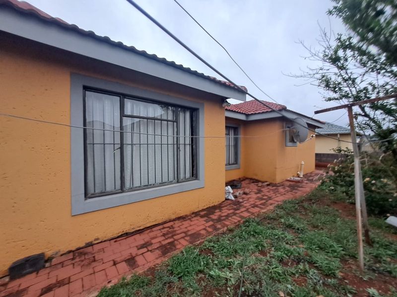 Rear exterior view of the house featuring plastered walls, tiled roof, and brick paved walkway leading along the side of the property.