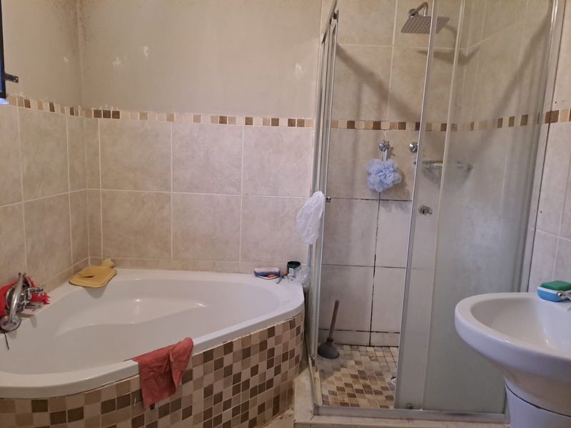 Bathroom featuring a corner bathtub, separate shower enclosure, and pedestal basin with tiled finishes requiring cosmetic updates.