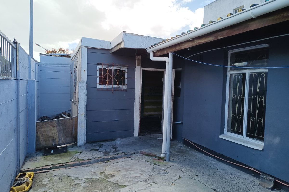 Rear exterior view of the property featuring a concrete patio area, security bars on windows, and boundary walling.