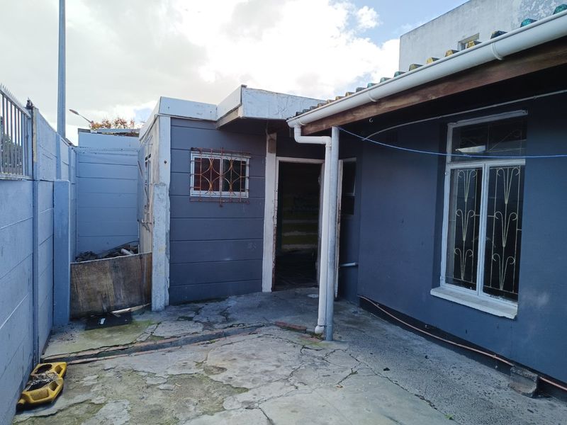Rear exterior view of the property featuring a concrete patio area, security bars on windows, and boundary walling.