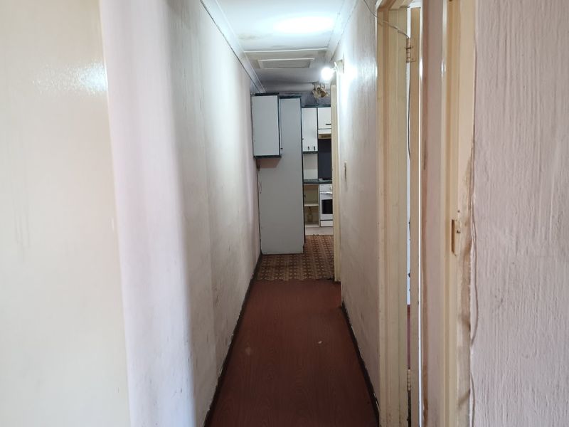 A narrow hallway with laminate flooring leading towards a kitchen area, showing signs of wear and requiring cosmetic updates.