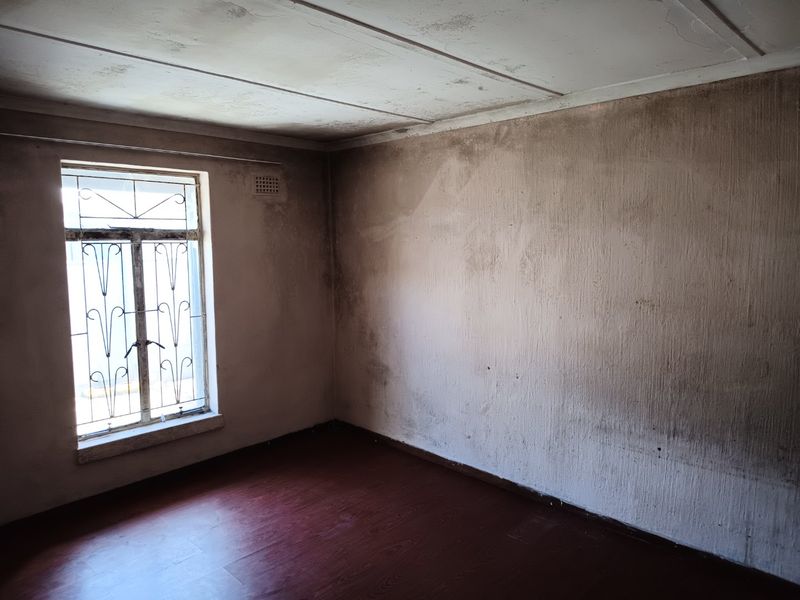 An empty bedroom featuring laminate flooring and a window with security bars, currently requiring significant wall and ceiling restoration.