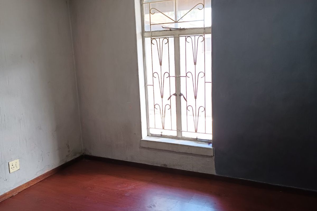 An empty bedroom featuring laminate flooring, a security gate on the window, and an air vent, requiring cosmetic updates to the ceiling and walls.