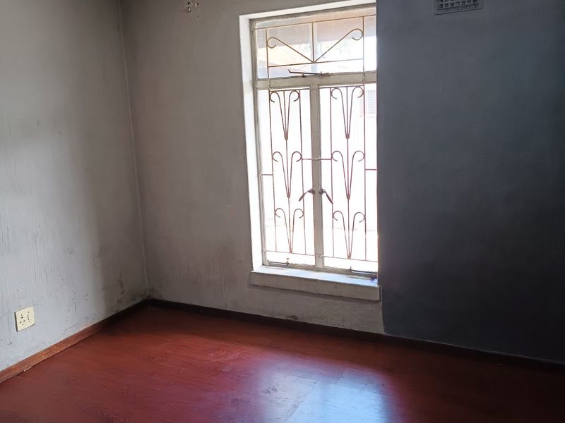 An empty bedroom featuring laminate flooring, a security gate on the window, and an air vent, requiring cosmetic updates to the ceiling and walls.