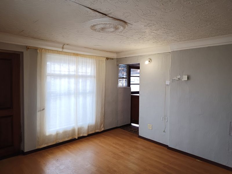 An empty living room featuring textured ceilings with a decorative rose, laminate flooring, and direct access to an exterior doorway with security gate.