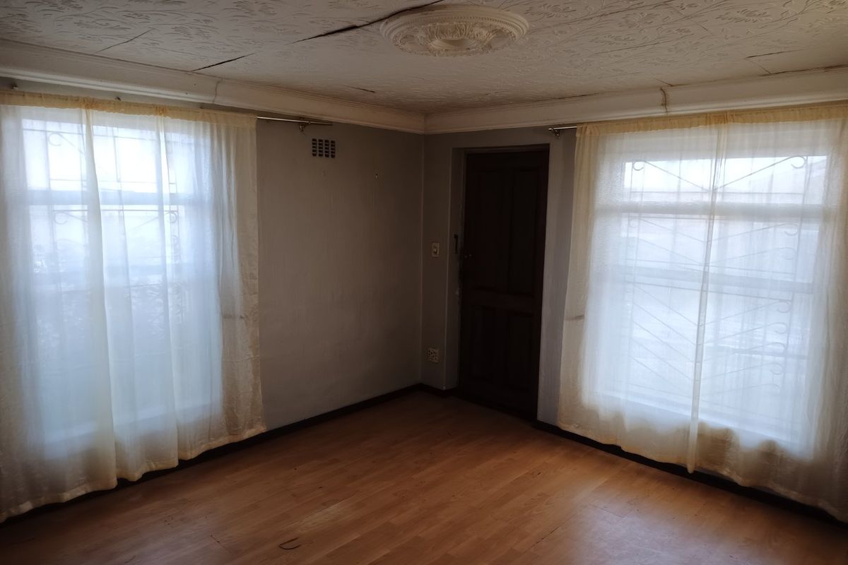 An empty living room featuring laminate flooring, textured ceiling tiles with a central rose, and windows fitted with security bars.