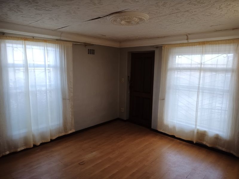 An empty living room featuring laminate flooring, textured ceiling tiles with a central rose, and windows fitted with security bars.