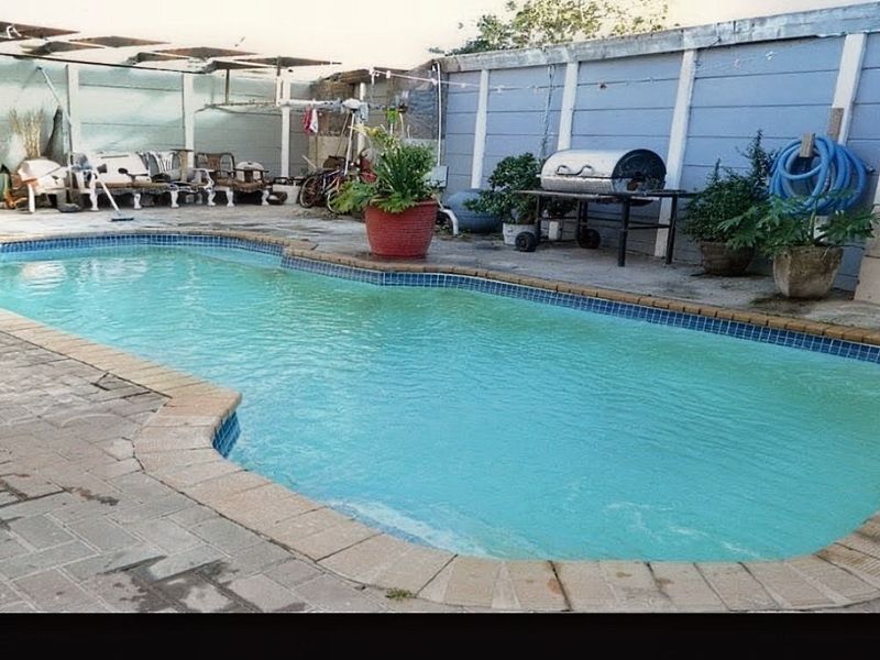 Outdoor pool area featuring a paved surround, boundary wall, and pergola structure, requiring maintenance and cosmetic updates to improve the overall aesthetic.