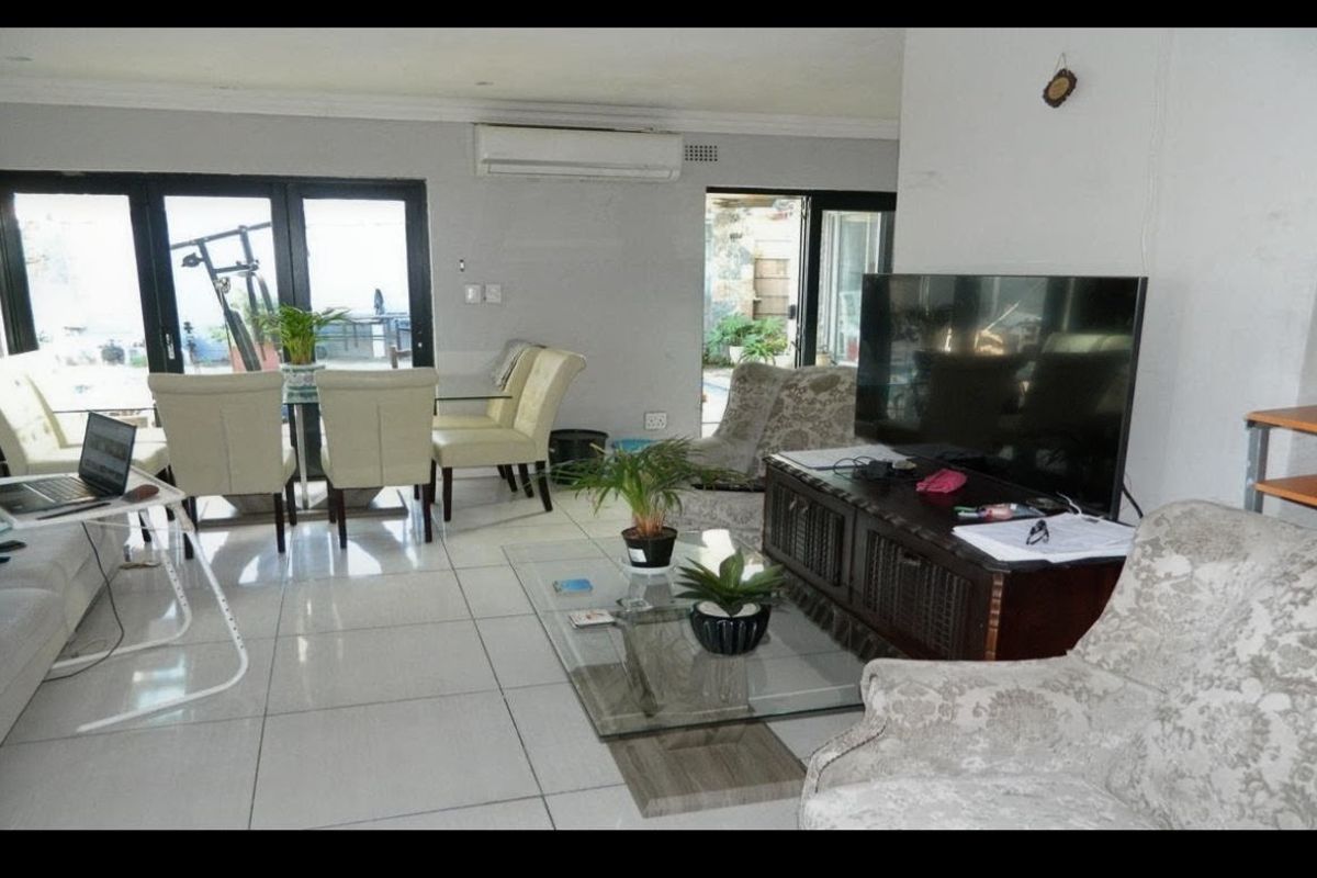 Open-plan living and dining area featuring large format floor tiles, split-system air conditioning, and sliding glass doors providing access to the outdoor space.