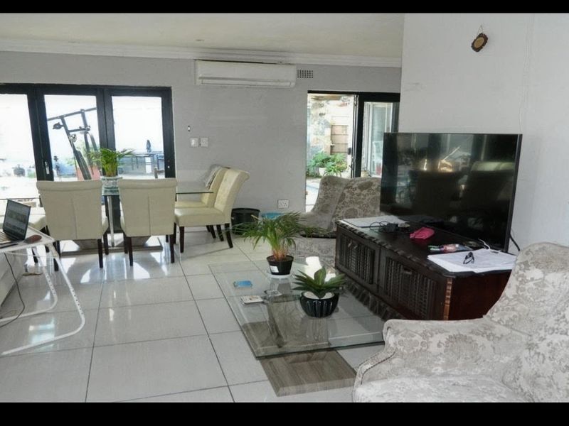 Open-plan living and dining area featuring large format floor tiles, split-system air conditioning, and sliding glass doors providing access to the outdoor space.