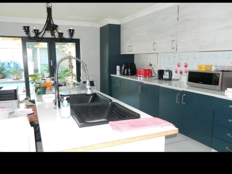 Modern kitchen featuring a central island with a double basin sink, stone countertops, two-tone cabinetry, and direct access to the outdoor patio area.