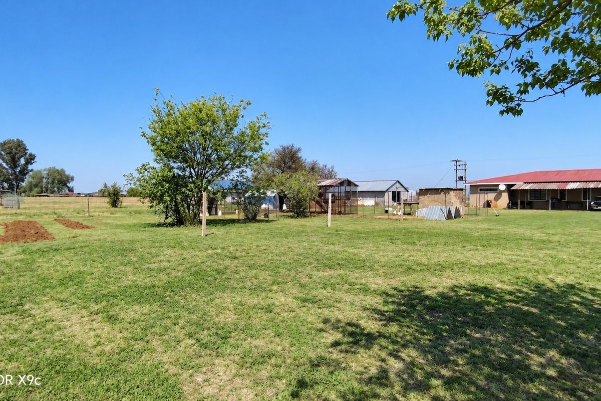 A spacious farm backyard featuring open grass areas, perimeter fencing, and various outbuildings under a clear blue sky.