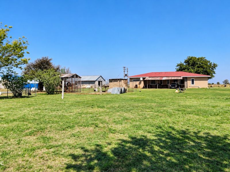 A wide view of the farm property featuring a main residence with a covered patio, surrounding outbuildings, and expansive open lawn space.