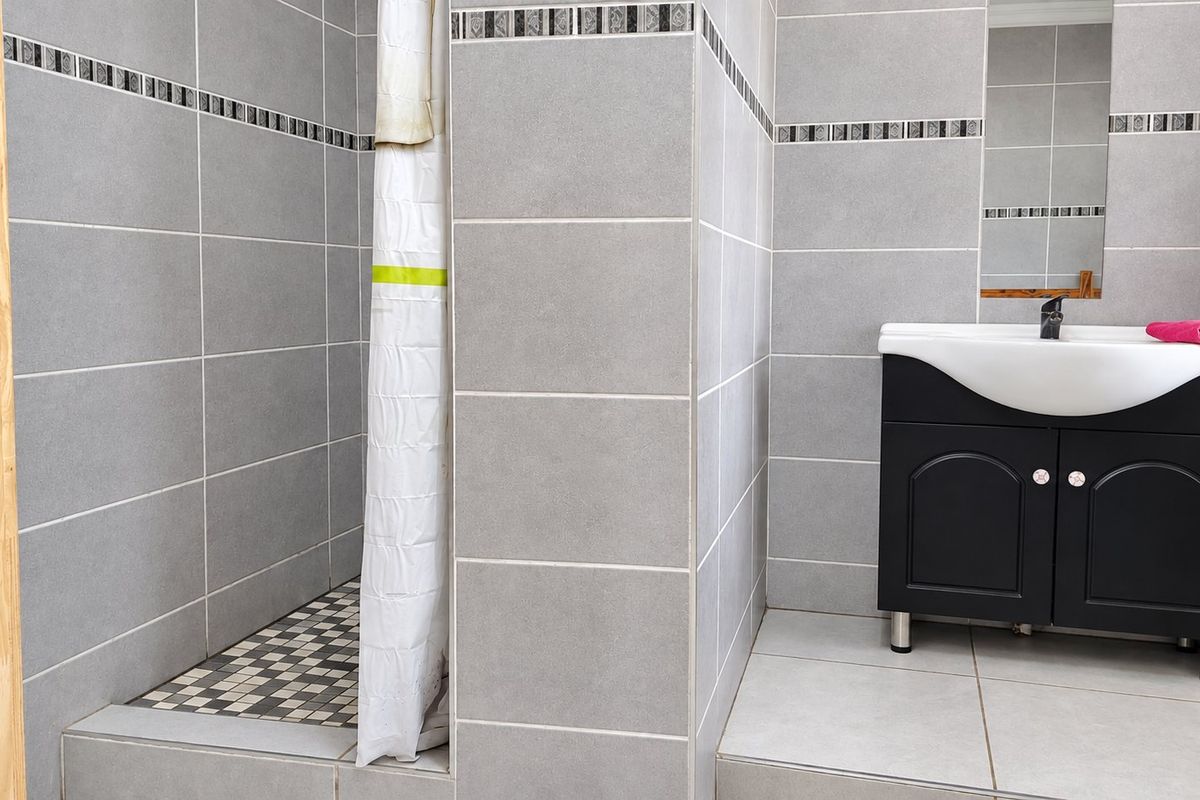 A modern bathroom featuring a walk-in shower with mosaic floor tiles and a vanity unit with a basin and mixer tap.