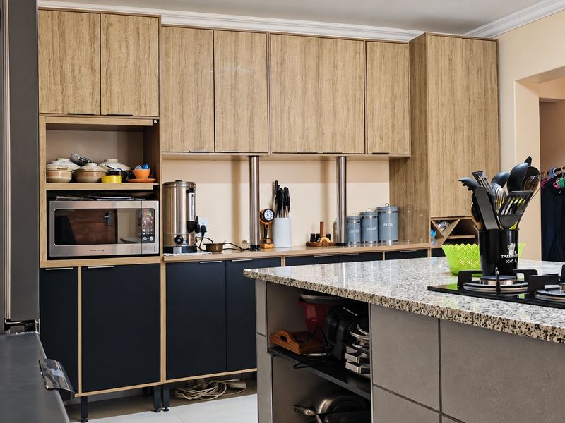 Modern kitchen featuring two-tone cabinetry, granite countertops, a central island with a gas hob, and integrated built-in oven.