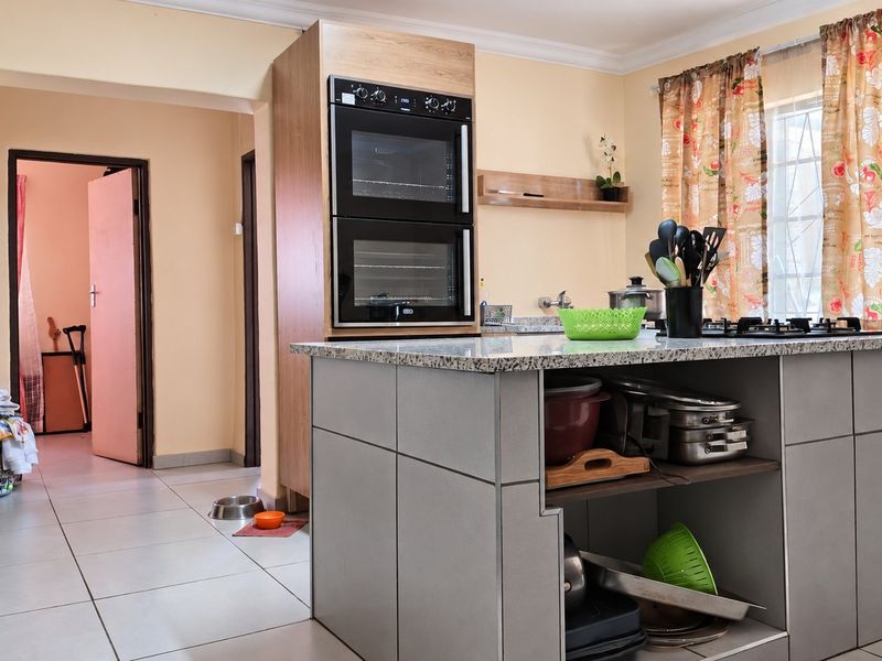 Functional kitchen featuring a central island with granite countertops, built-in double oven, and gas hob, offering practical workspace and storage.