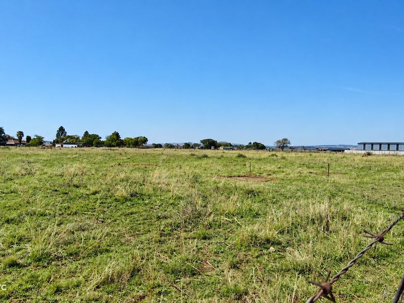 A wide-angle view of open farm pasture land enclosed by a barbed wire fence under a clear blue sky.