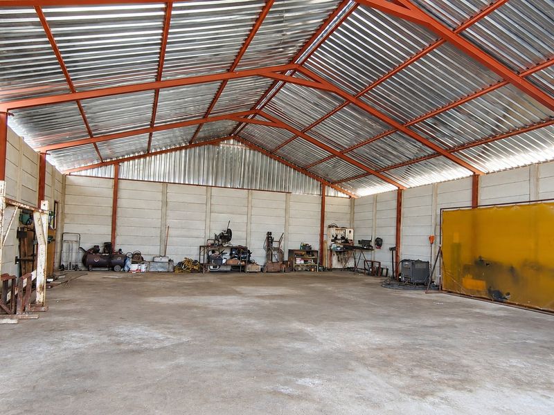 Spacious industrial utility shed featuring a high-pitched corrugated metal roof, steel frame construction, and durable concrete flooring, suitable for workshop or storage use.