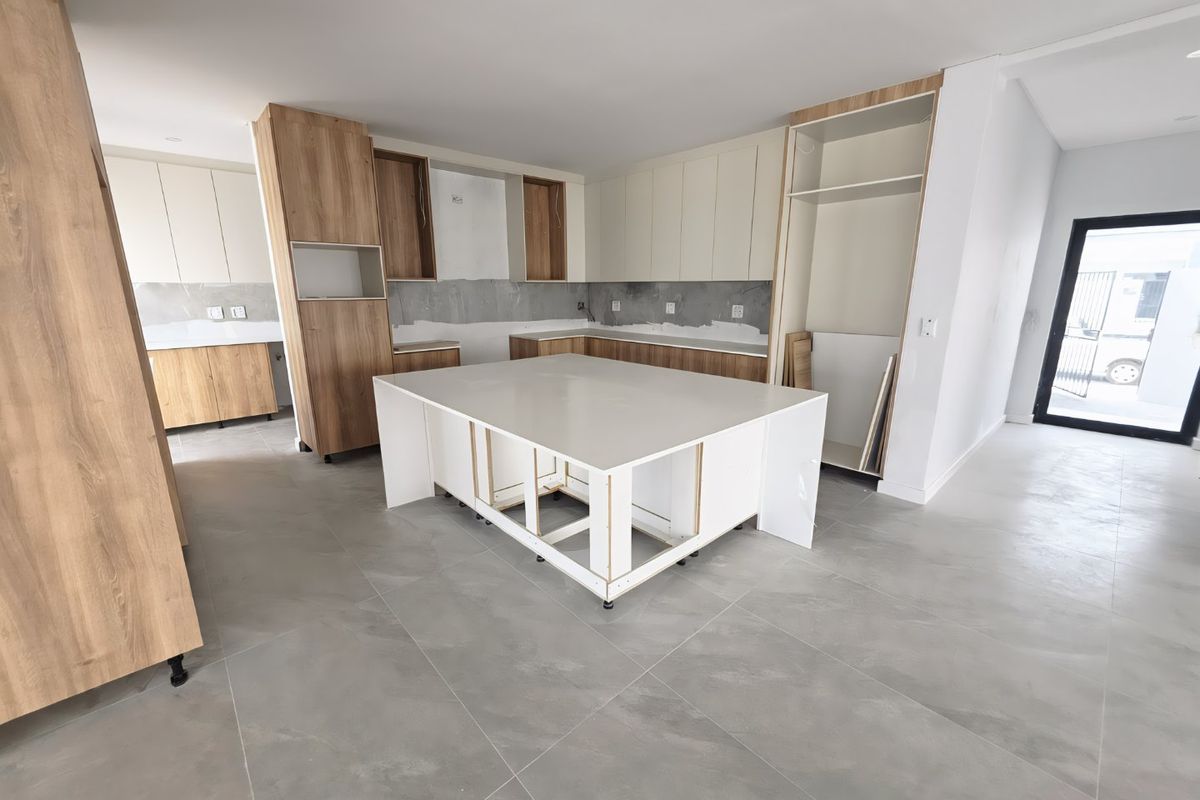 An unfinished modern kitchen featuring a central island, light wood and white cabinetry, and large format floor tiles, currently awaiting final installation and finishes.