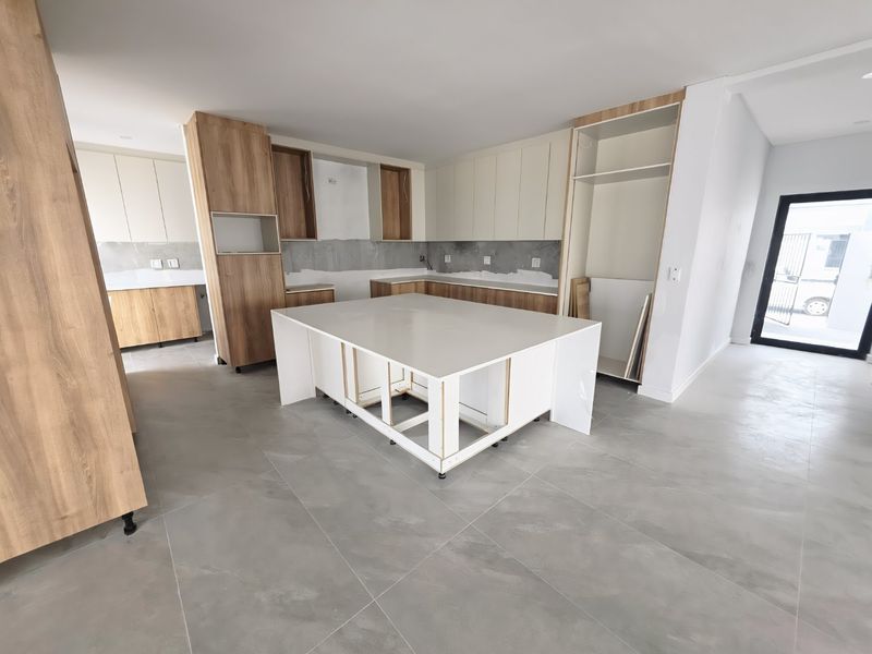 An unfinished modern kitchen featuring a central island, light wood and white cabinetry, and large format floor tiles, currently awaiting final installation and finishes.