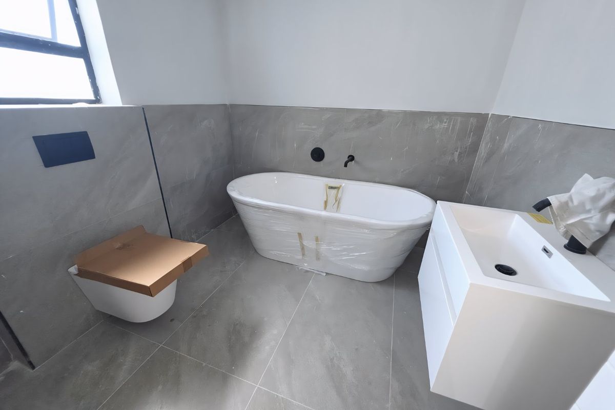 Modern bathroom featuring a freestanding bathtub, wall-hung toilet, and sleek vanity cabinet with contemporary grey floor-to-wall tiling.