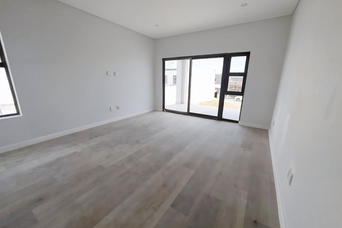A bright, modern, and empty living area featuring light-toned laminate flooring, recessed lighting, and large sliding glass doors leading to an outdoor space.