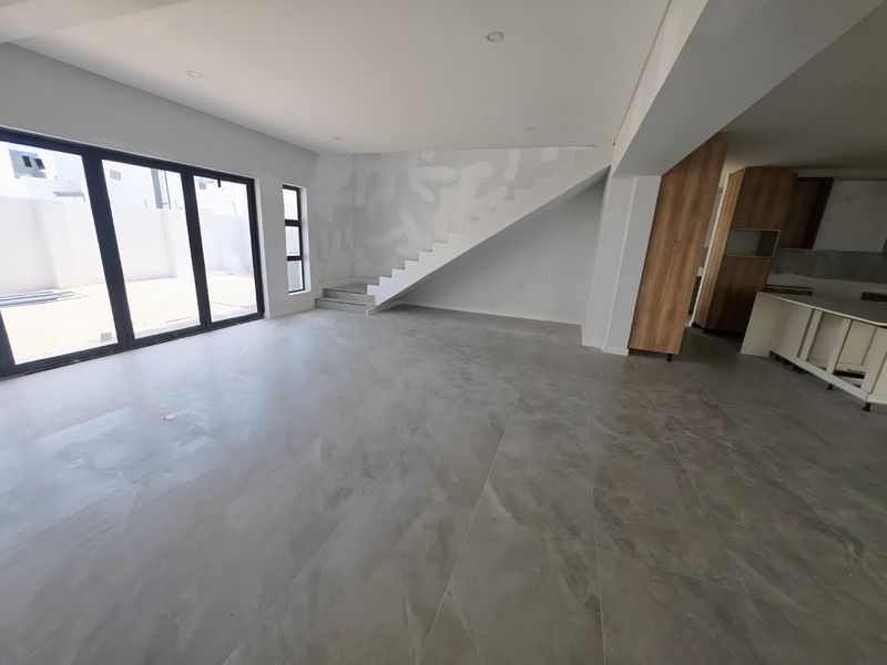 Spacious open-plan living area featuring large sliding doors, tiled floors, and an integrated kitchen, currently in a semi-finished state awaiting final touches.