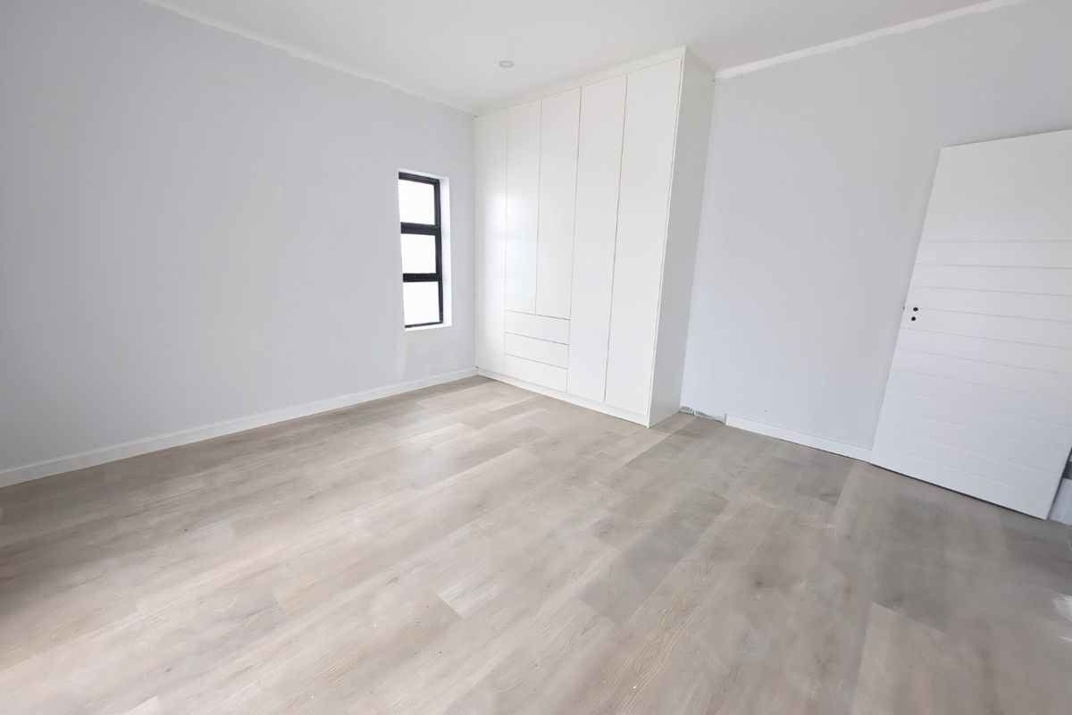 A bright, empty bedroom featuring modern laminate flooring, built-in white cupboards, and a clean, neutral aesthetic ready for personalization.