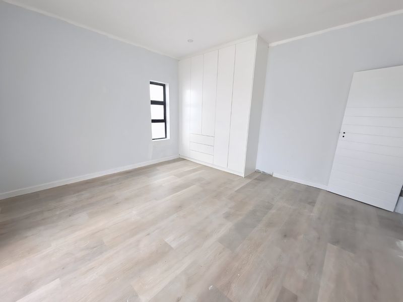A bright, empty bedroom featuring modern laminate flooring, built-in white cupboards, and a clean, neutral aesthetic ready for personalization.