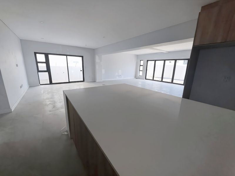Spacious open-plan living and kitchen area featuring a central island, large sliding glass doors, and modern recessed lighting, currently in an unfinished state.