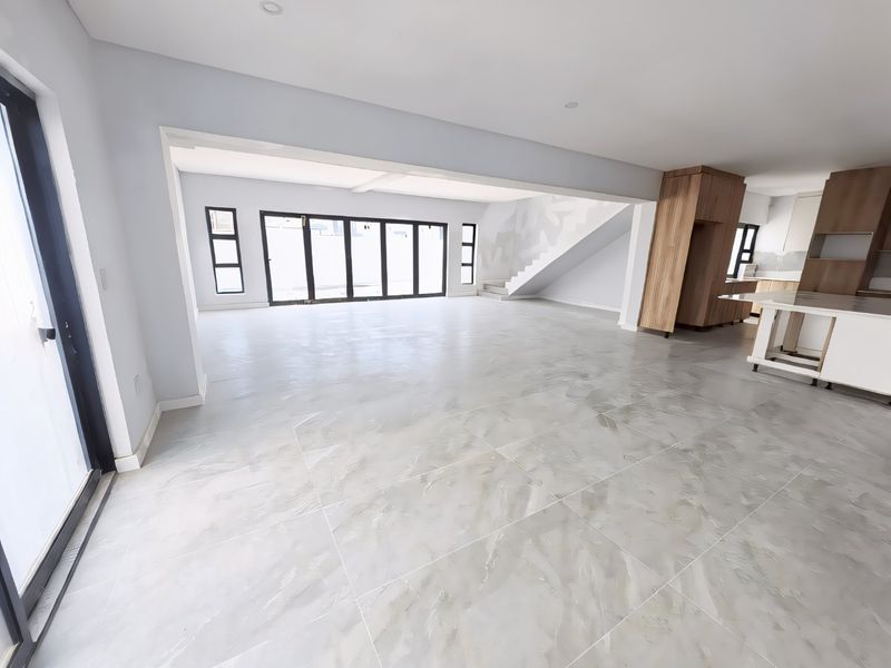 Spacious open-plan living and kitchen area featuring large format floor tiles, modern built-in cabinetry, and expansive sliding glass doors leading to the exterior.