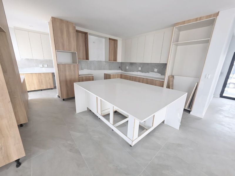 An unfinished modern kitchen featuring light wood cabinetry, a large central island, and neutral floor tiles, currently awaiting final installation and finishing touches.