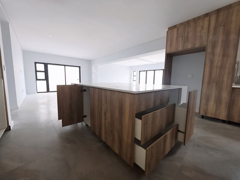 Modern open-plan kitchen area featuring a central island with wood-finish cabinetry, stone countertops, and large sliding doors leading to the exterior.
