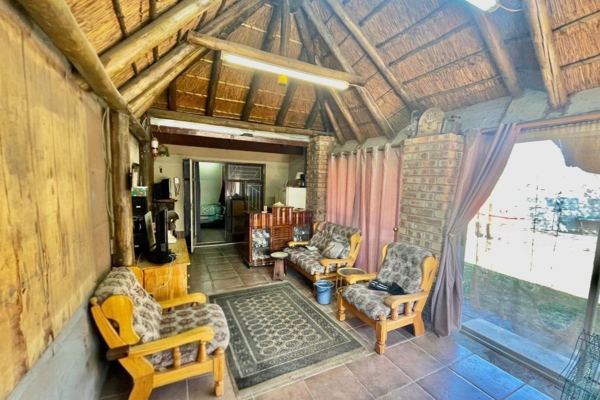 Rustic living area featuring a traditional thatched roof with exposed timber rafters, exposed brick pillars, and tiled flooring with access to the outdoors.