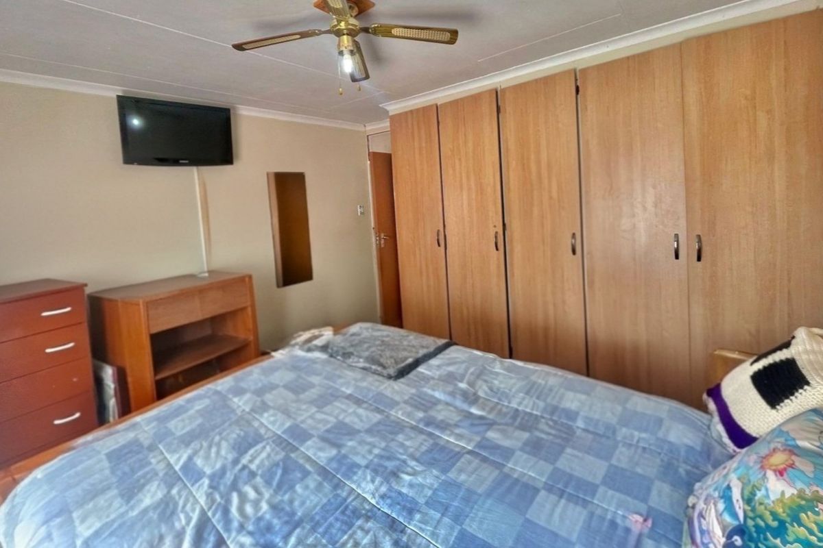 A functional bedroom featuring extensive built-in wooden cupboards and a ceiling fan, offering practical storage and climate control.