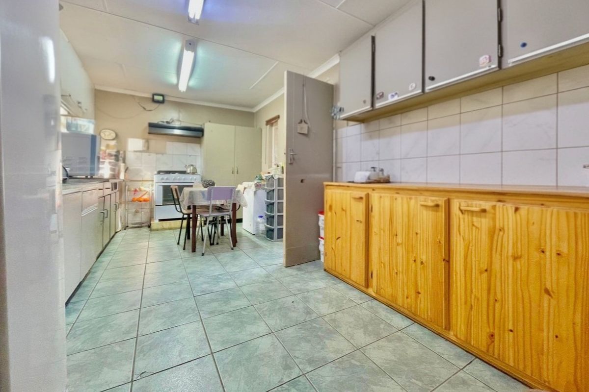 A functional kitchen featuring wooden cabinetry, tiled flooring, and a tiled backsplash, offering a practical layout with a freestanding stove and extractor fan.
