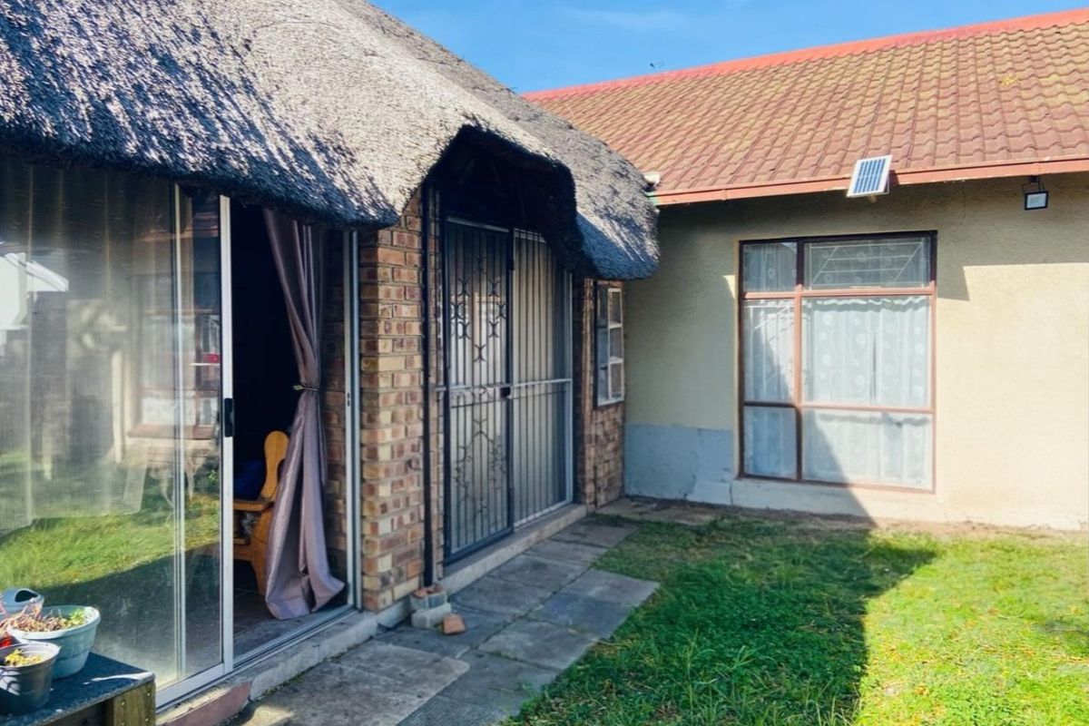 Rear view of the property featuring a combination of thatched and tiled roofing, sliding glass doors with security gates, and a small garden area.