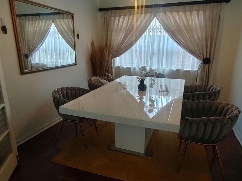A well-lit dining room featuring neutral wall finishes, dark flooring, and window treatments.