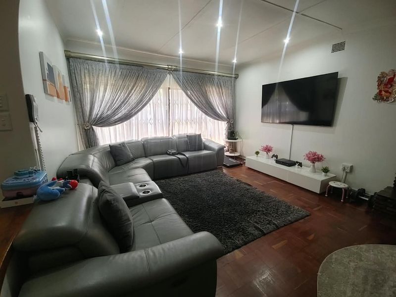 A comfortable living room featuring warm parquet flooring, recessed downlighting, and large windows fitted with security gates and elegant curtains.