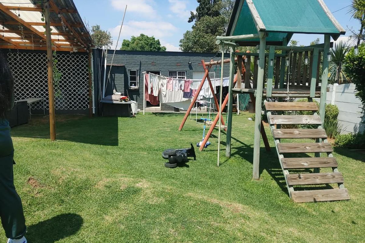 A private rear garden featuring a lawn area, a timber pergola structure, and a dedicated play area with a wooden climbing frame.