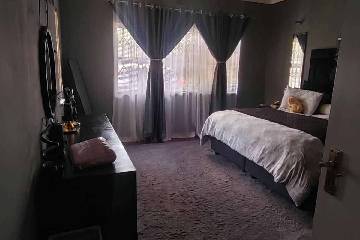 A spacious bedroom featuring dark wall finishes, an integrated air conditioning unit, and a security gate on the window.