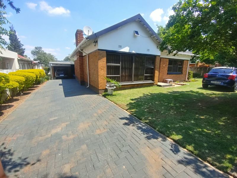 Front view of a brick house featuring a paved driveway, carport, and a well-maintained front garden.