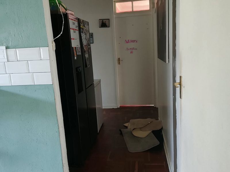 A narrow hallway featuring parquet flooring, a transom window above the door, and a partial view of a kitchen area with subway tile backsplash.