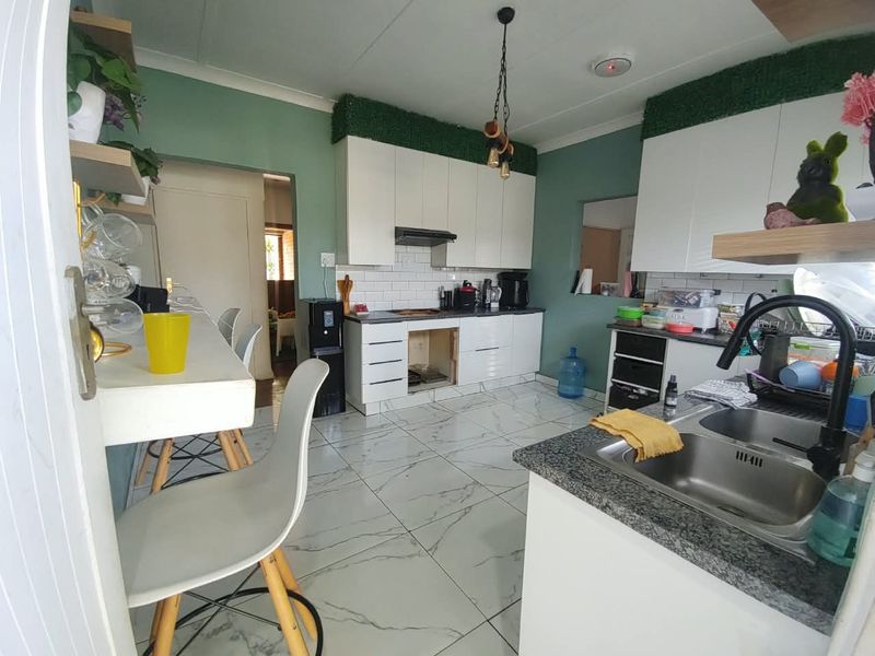 A functional kitchen featuring white cabinetry, subway tile backsplash, marble-look floor tiles, and a breakfast bar, with a missing cabinet door noted.