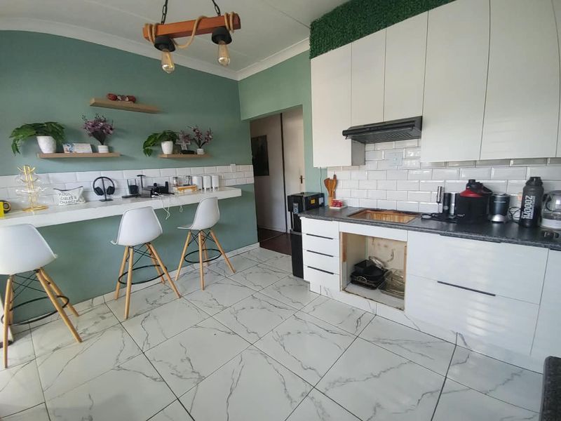 Kitchen featuring white cabinetry, subway tile backsplash, marble-look floor tiles, and a breakfast bar. Note the missing cabinet door under the counter.