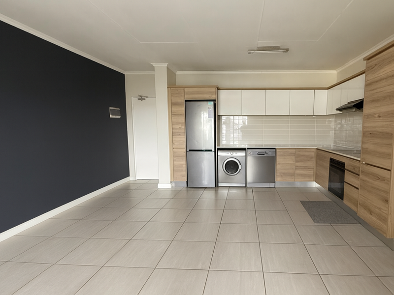 Modern open-plan kitchen featuring light wood and white cabinetry, integrated appliances, subway tile backsplash, and neutral tiled flooring in a spacious living area.