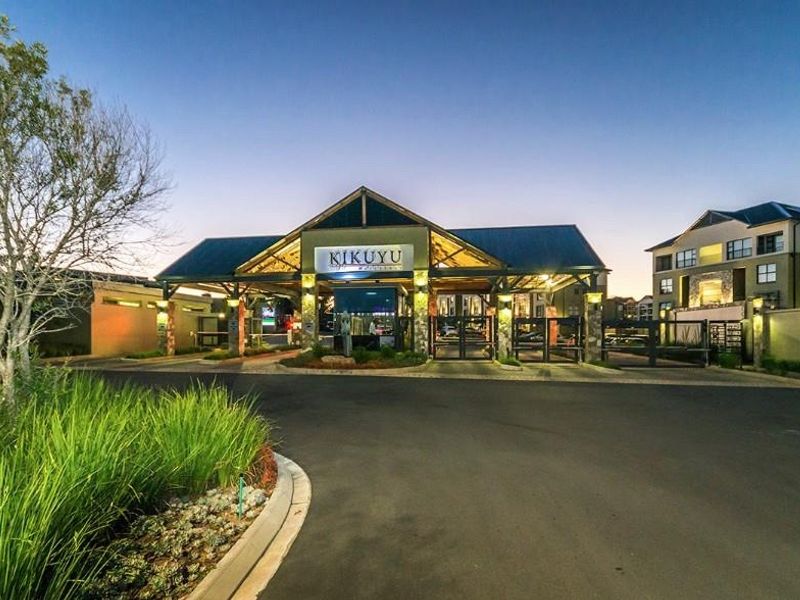 The main entrance and security gatehouse of the Kikuyu apartment complex, featuring modern architectural design, paved driveway, and landscaped surroundings at dusk.