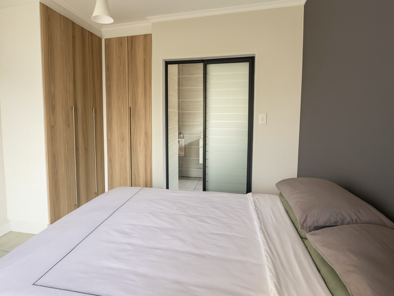 A well-maintained bedroom featuring modern wood-finish built-in cupboards and a sliding door leading to an en-suite bathroom.