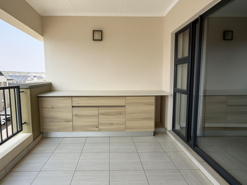 A clean, modern balcony featuring tiled flooring, a built-in storage cabinet, and a metal balustrade with views of the surrounding complex.